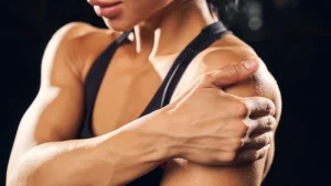Mulher atleta segurando o ombro após treino intenso, representando a recuperação muscular e os cuidados com o corpo no pós-exercício.